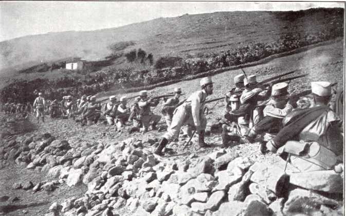 Foto que muestra una batalla, puede verse una hilera de soldados con rodilla en tierra y disparando fusiles.
